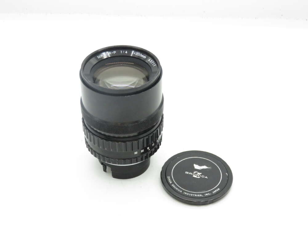 IMG_0663 Black Nikkor-P 200mm f/4 camera lens with lens cap on a white background.