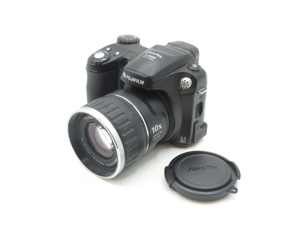 IMG_0574 A Fujifilm FinePix S5200 camera with a detachable lens cap beside it.