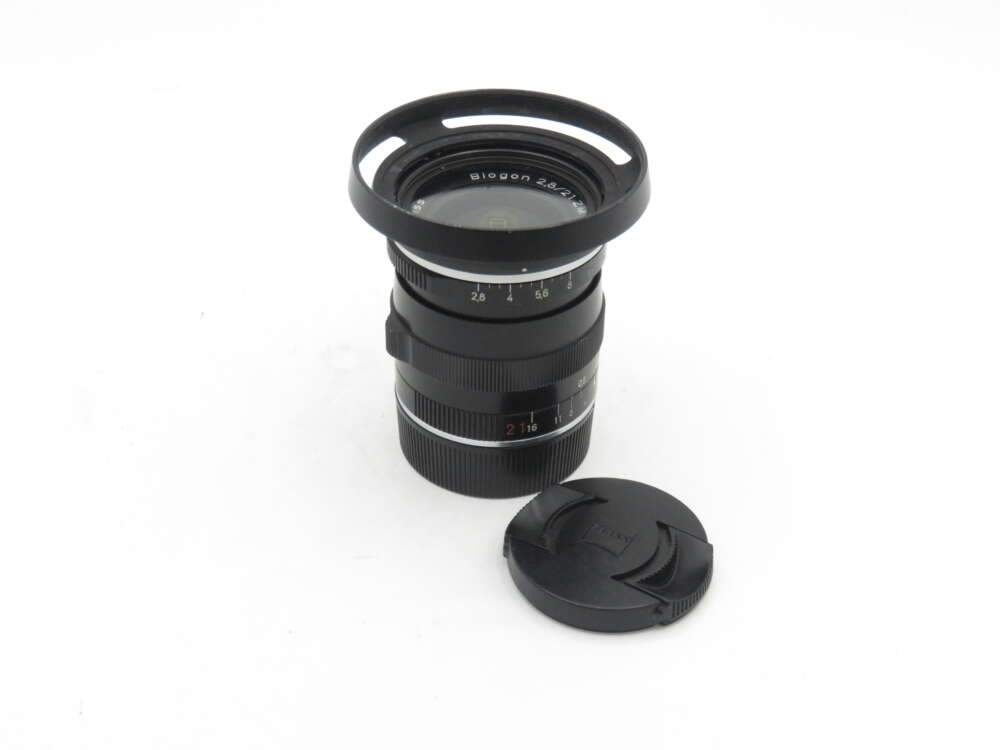 IMG_0603 Camera lens with lens hood attached, next to a detached lens cap on a white background.