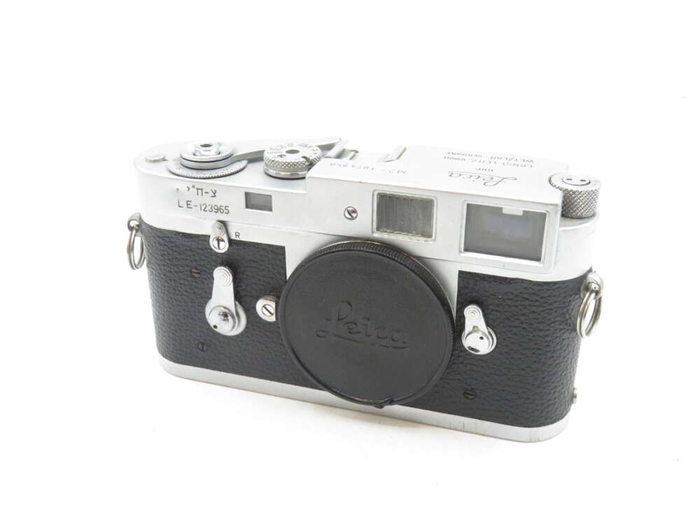 IMG_0610 Vintage Leica film camera with black leatherette body and silver metal top, showing dials, viewfinder, and lens cap with "Leica" logo.