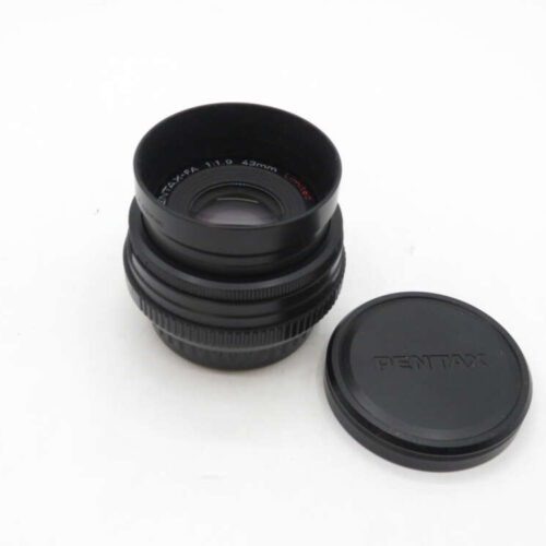 A Pentax camera lens next to a detached lens cap, on a white background.