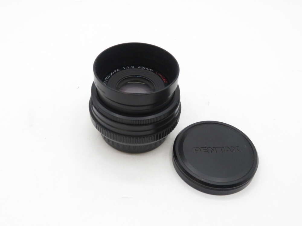 IMG_0677 A Pentax camera lens next to a detached lens cap, on a white background.