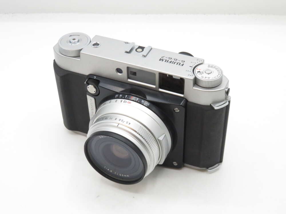 IMG_0439 A silver and black Fujifilm camera with a large lens, featuring various dials and a viewfinder on a white background.