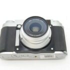 A vintage-style camera with a black grip and a silver body, featuring an EBC Fujinon lens with a focal length of 55mm.