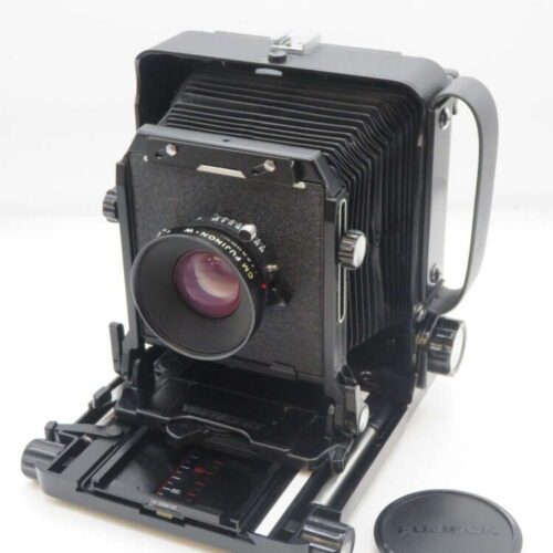 Large format folding field camera with bellows and a Fujinon lens, accompanied by a detached lens cap.