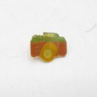 Enamel pin in the shape of a Pentax camera with an orange body and green details.