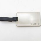 Rectangular silver luggage tag with "SONY" engraved in the bottom right corner and an attached black leather strap.
