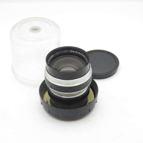 A camera lens with a black and silver body, placed in a black base and next to a clear plastic cover.