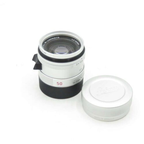Leica 50mm lens with a detached lens cap placed nearby on a white background.