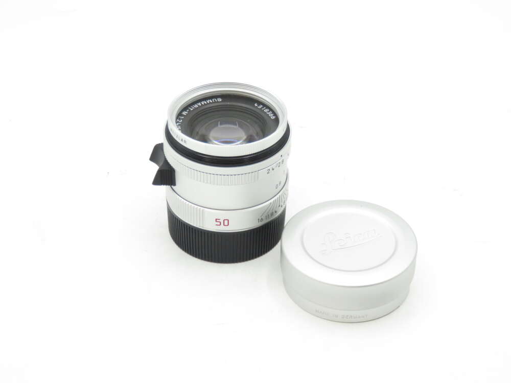 IMG_1562 Leica 50mm lens with a detached lens cap placed nearby on a white background.