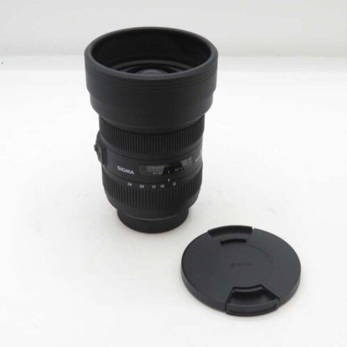 Sigma camera lens with the lens cap placed beside it on a white surface.