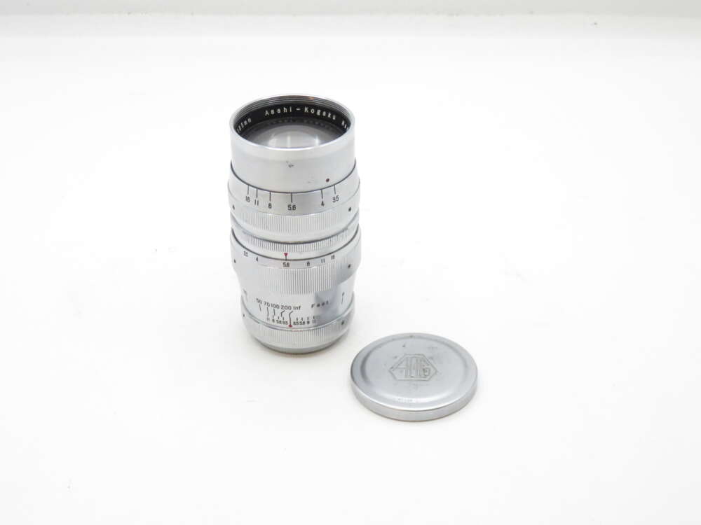 IMG_1964 Silver Asahi-Kogaku camera lens with detached lens cap on a white background.