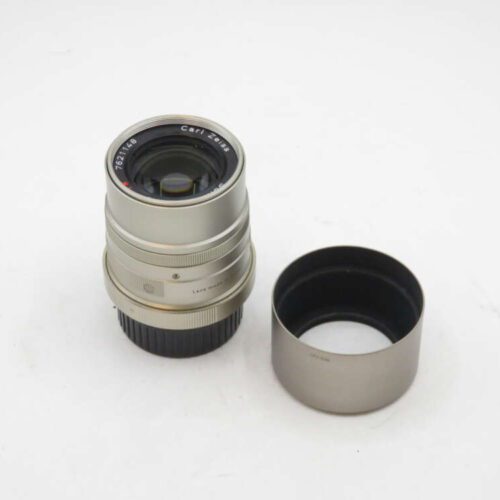 Silver camera lens and its detached hood on a white surface.