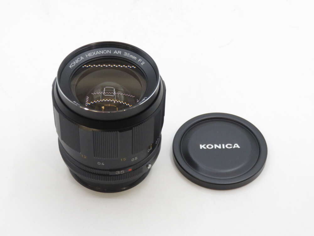 IMG_2756 Konica Hexanon AR 35mm F2 camera lens with lens cap beside it.