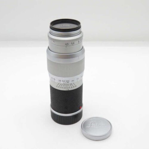 Silver Leica camera lens with black grip, next to a detached silver lens cap.