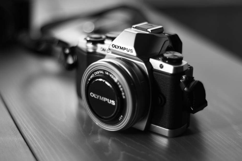 Black and white photo of an Olympus OM-D digital camera on a wooden surface.