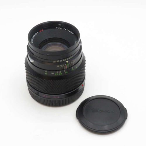 Zenzanon MC camera lens with a detachable lens cap placed beside it.
