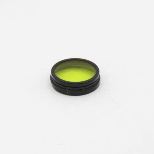 A black camera lens filter with a yellow tint, placed on a white surface.
