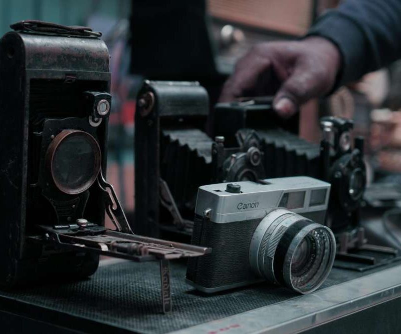 A collection of vintage cameras displayed on a table, with a hand reaching towards one.