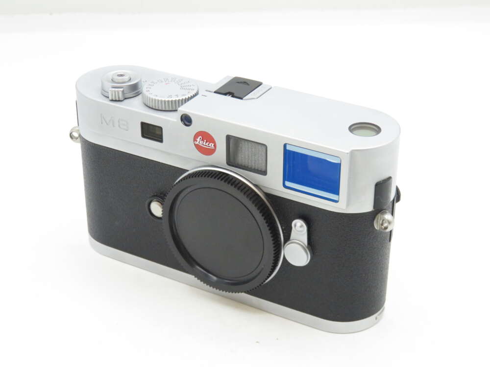 IMG_0345 Leica M8 digital rangefinder camera with a black lens cap on a white surface.