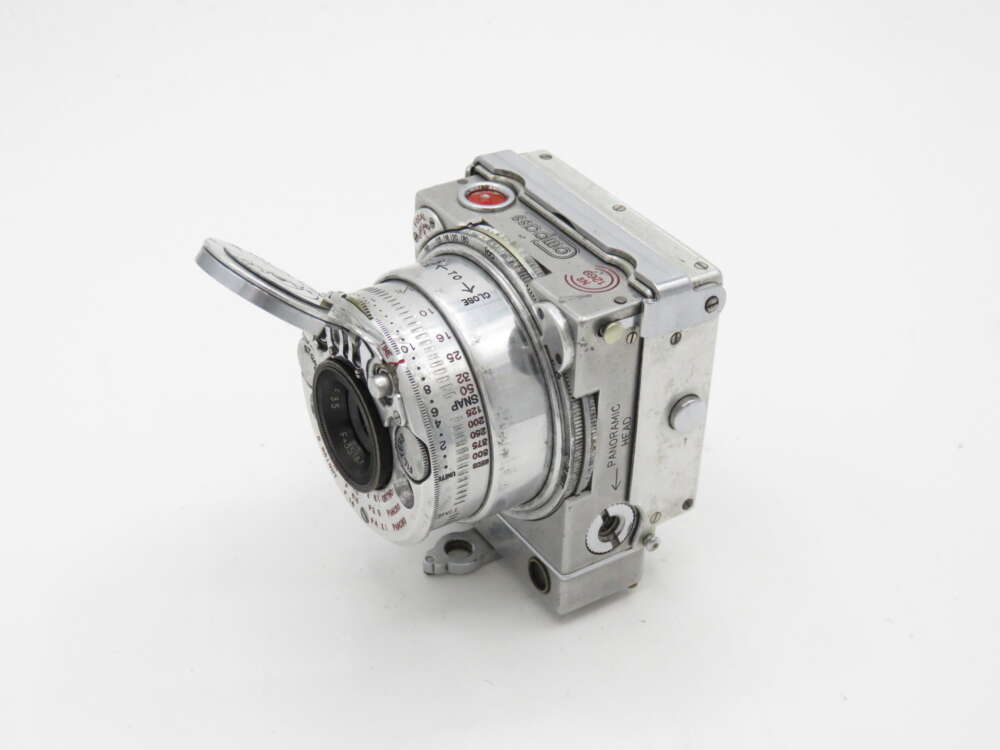 Vintage metal camera with a protruding lens and various dials and markings.