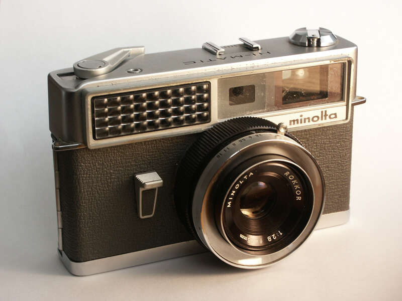 A vintage Minolta camera with a Rokkor lens, featuring a rectangular body and textured grip.