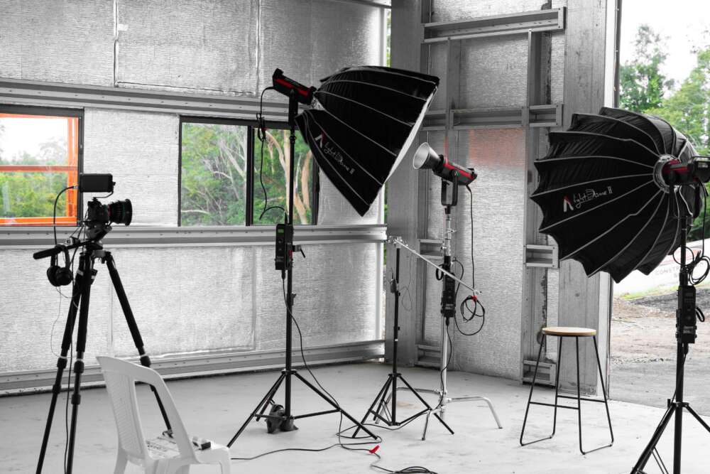 Photography studio setup with lighting equipment, camera on a tripod, and a stool.