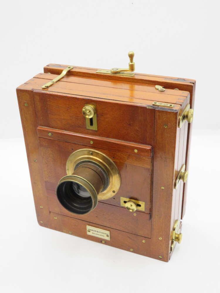 IMG_0088 An antique wooden box camera with brass fittings and a prominent lens, featuring a polished wooden exterior and metal knobs for adjustments.