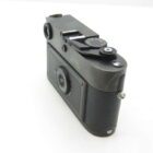 Black vintage camera with a textured grip, showing the back and top view including a dial and film advance lever.