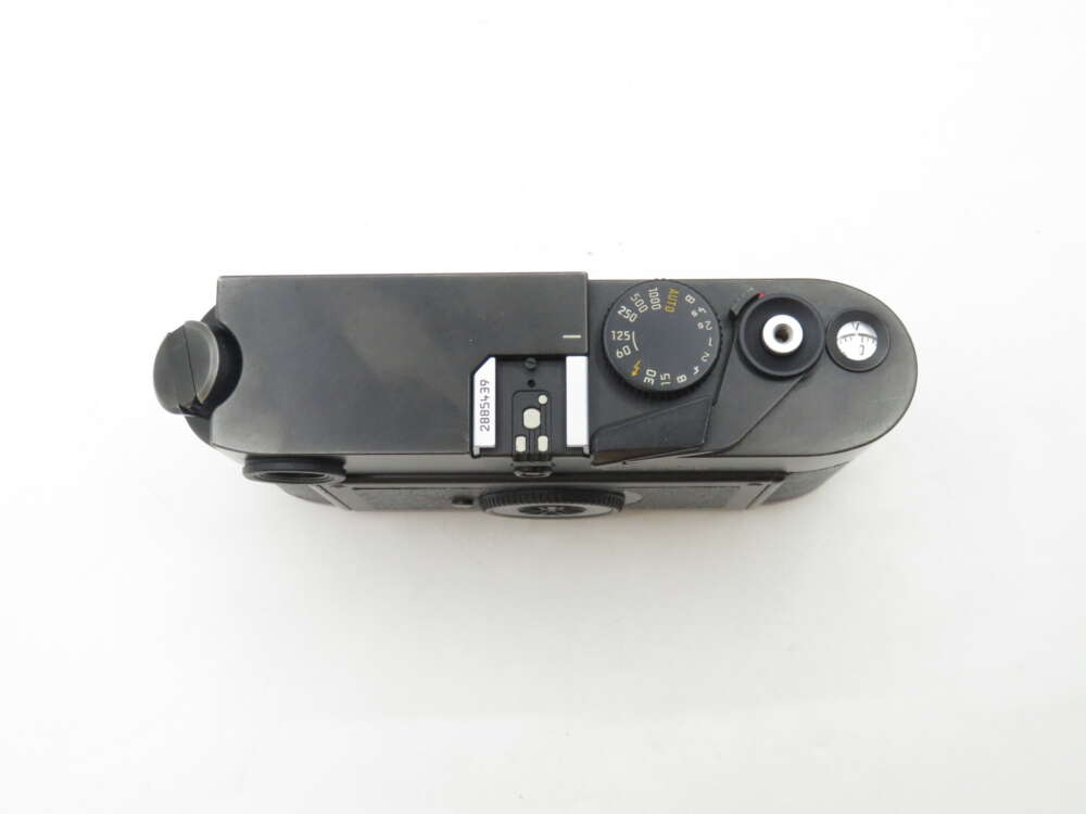 Top view of a black film camera, showing the shutter speed dial, viewfinder, and film advance lever.