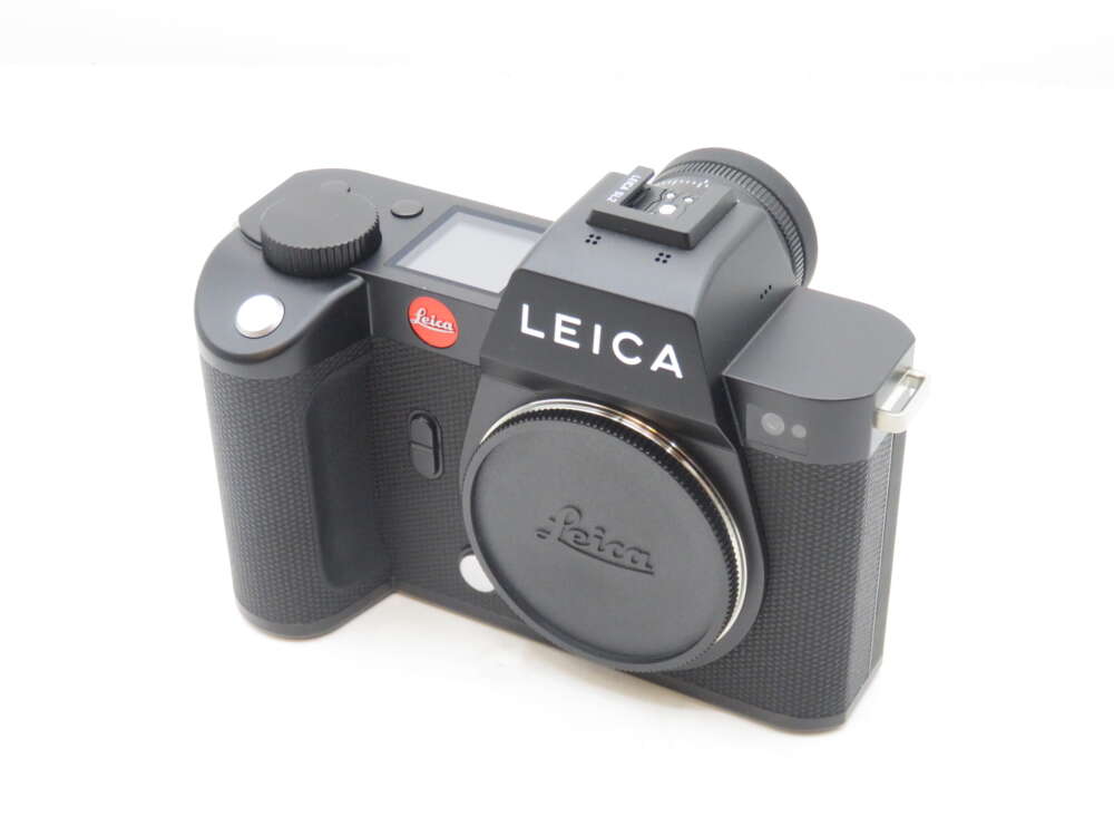 IMG_0413 A black Leica digital camera with a simple design, featuring a detachable lens cap and textured grip.