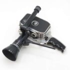 A vintage movie camera with a black matte finish, featuring a long lens and a pistol grip handle, displayed on a white background.
