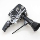 A vintage handheld film camera with a black grip handle and a long black lens attachment, featuring silver metal accents and a wheel dial on a plain white background.
