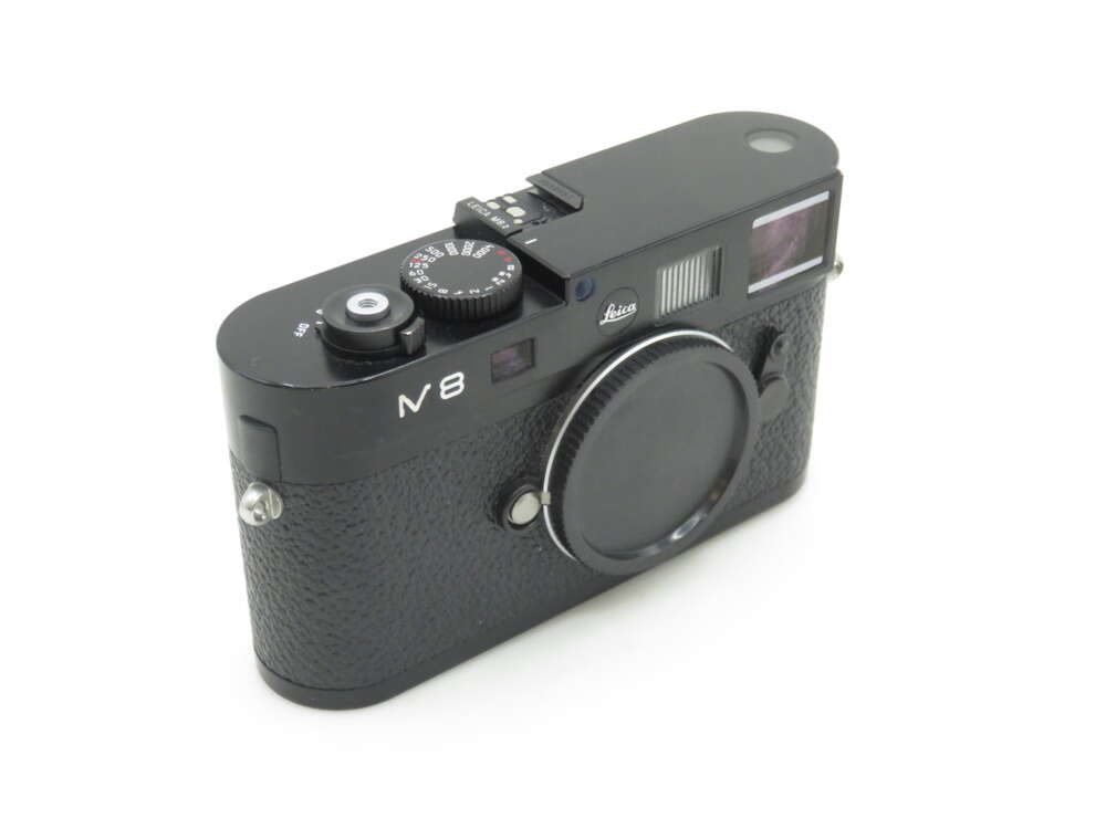 A Leica M8 camera with a black body and textured grip, featuring a silver dial and viewfinder on the top, set against a plain white background.
