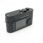 A black Leica camera with a textured grip, viewfinder, and a screen on the back, displaying control buttons labeled Play, Delete, Protect, Info, and Set. The camera is angled to show the top with dials and buttons, including an ISO adjustment dial.