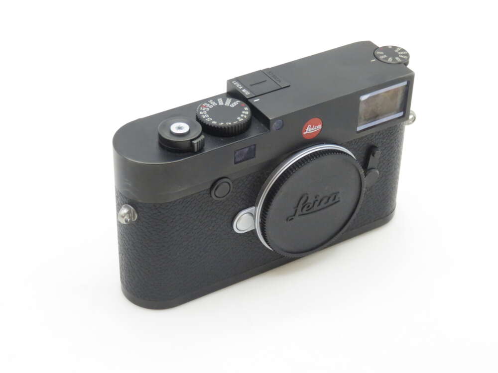 A black Leica camera with various control dials and a lens cap displaying the Leica logo, placed on a white surface.
