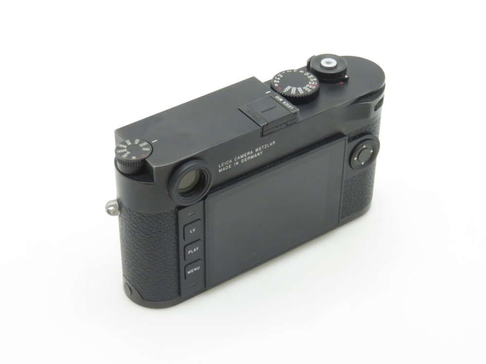 A black camera with a textured grip, featuring a rear LCD screen and various control dials on top, labeled "LEICA CAMERA WETZLAR MADE IN GERMANY."