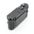 A black digital camera viewed from the back and top, showing its LCD screen and control dials, including the shutter speed and ISO settings.