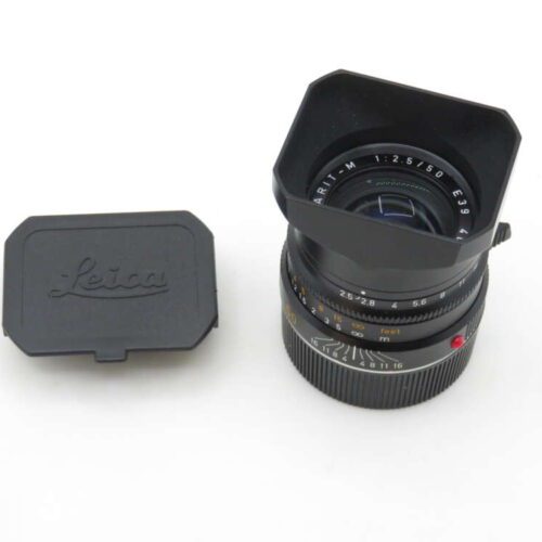 A Leica 50mm camera lens with a lens hood, placed next to its rectangular black lens cap, on a white background.