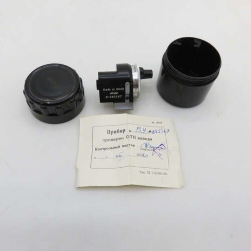 A round black device with a label indicating 'Made in USSR' and the serial number, disassembled into three parts on a white surface, alongside a small piece of paper featuring text and handwriting in Russian.