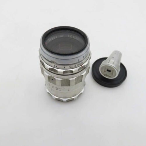 A vintage Travenar 135mm camera lens with a silver metallic finish, accompanied by an accessory part on a white background.