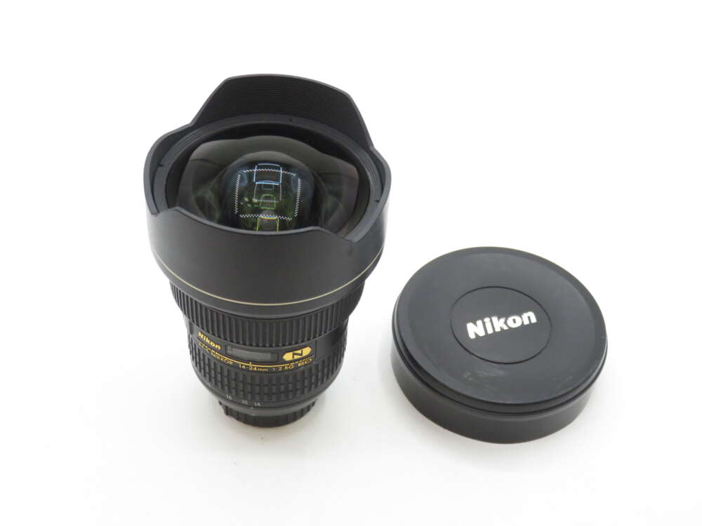 IMG_1048 A Nikon ultra wide-angle lens with a lens cap beside it, featuring a prominent front element and black exterior design with gold lettering.