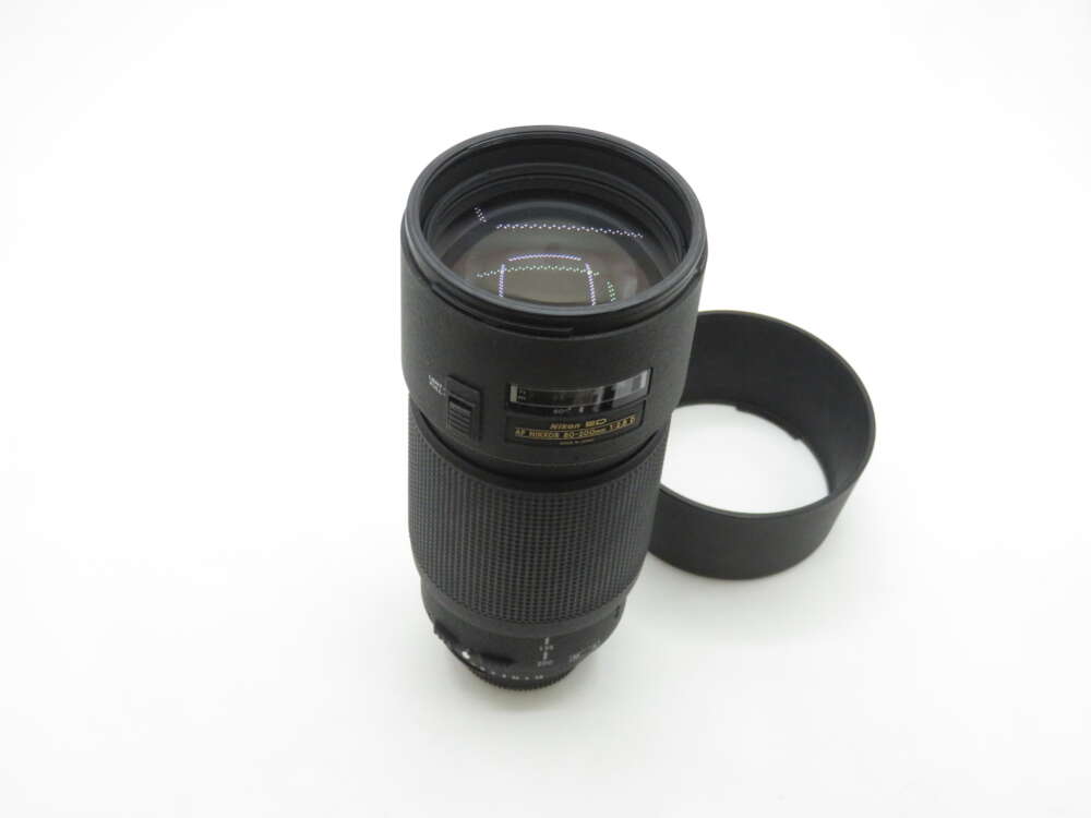 IMG_1074 A telephoto camera lens standing upright next to its detached lens hood on a white background.