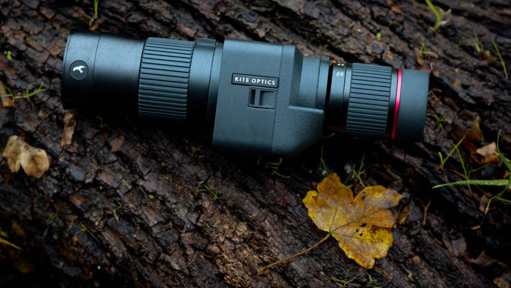 A Kite Optics telescope lying on a tree trunk with a yellow leaf nearby.