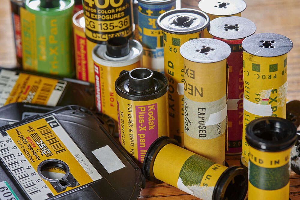 A collection of various vintage film rolls and cartridges, including Kodak and other brands, arranged on a wooden surface.