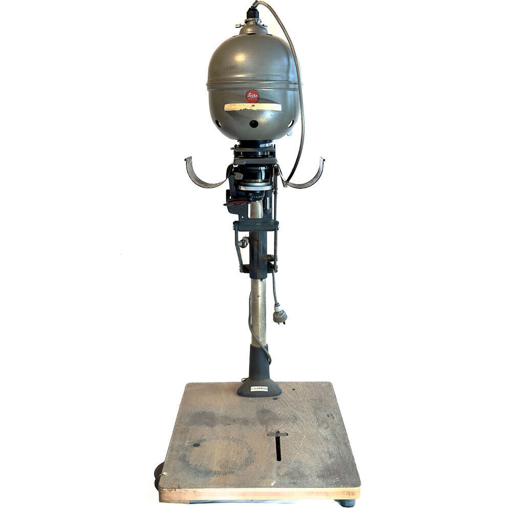 003 A vintage dry cleaning press with a metallic body, mounted on a wooden base. The machine features a large, round top chamber and a lever mechanism, indicative of older industrial equipment.
