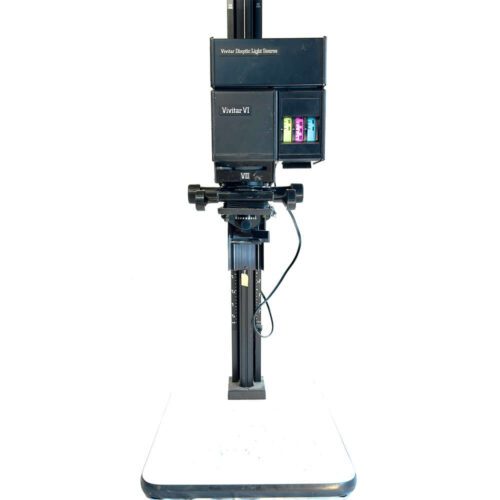 A Vivitar VI enlarger with a black body, featuring adjustment knobs and a colour panel for photographic darkroom use, mounted on a vertical track and positioned on a white base.