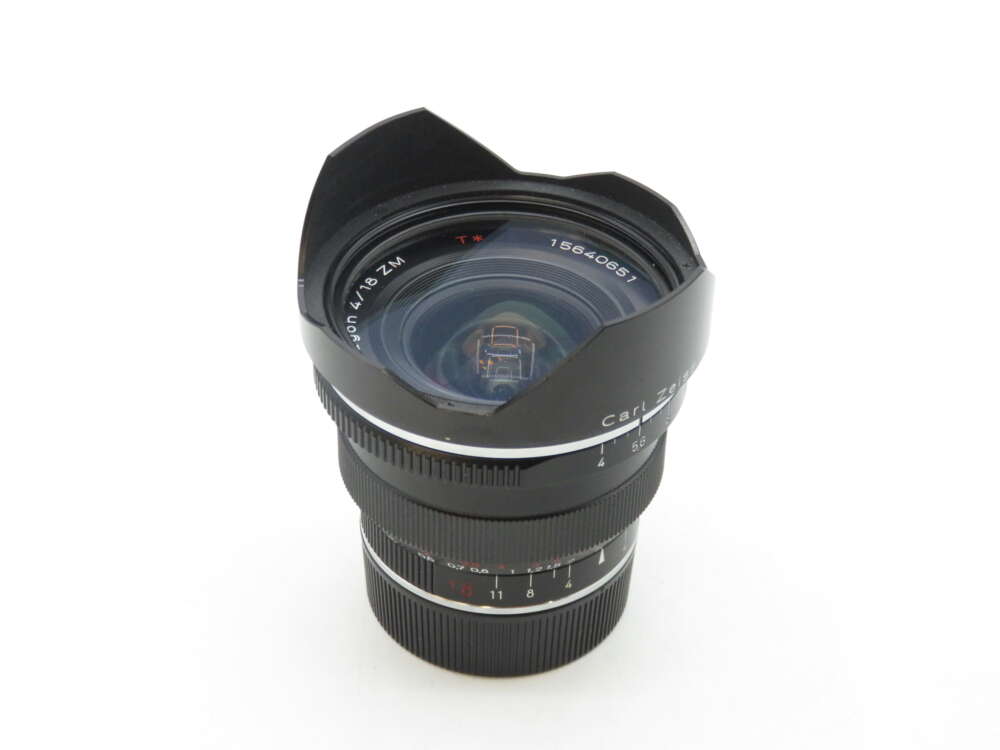 IMG_1340 A Carl Zeiss Distagon T* 18mm f/4 lens with a wide-angle hood, featuring focus and aperture adjustment rings on a white background.