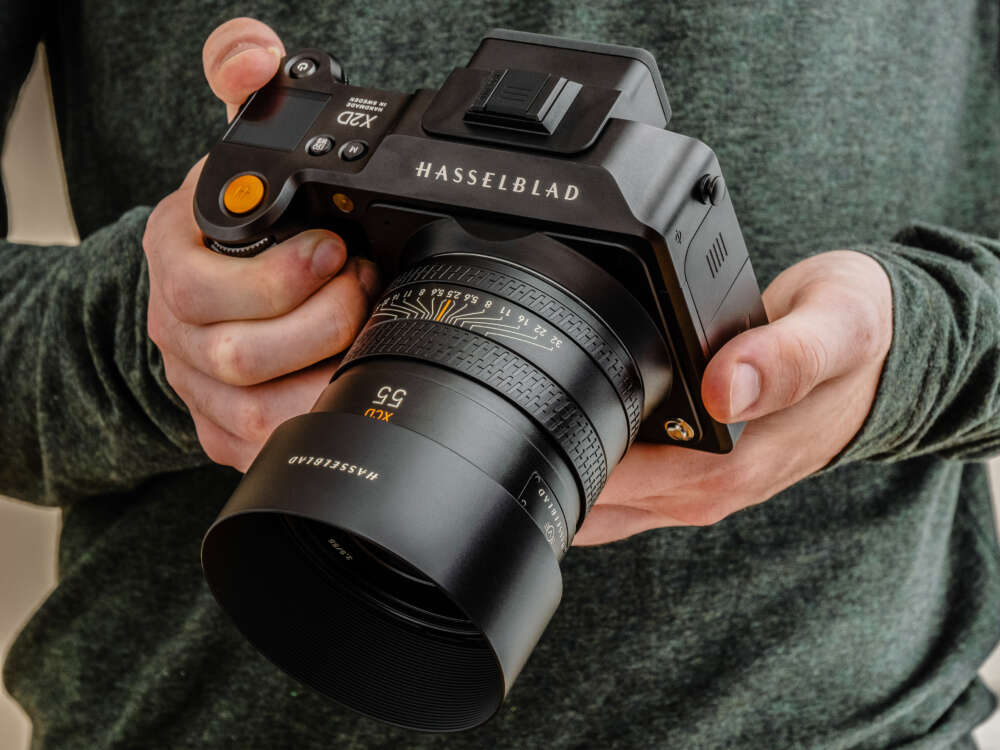 A person holding a Hasselblad X2D camera with a 55mm XCD lens.