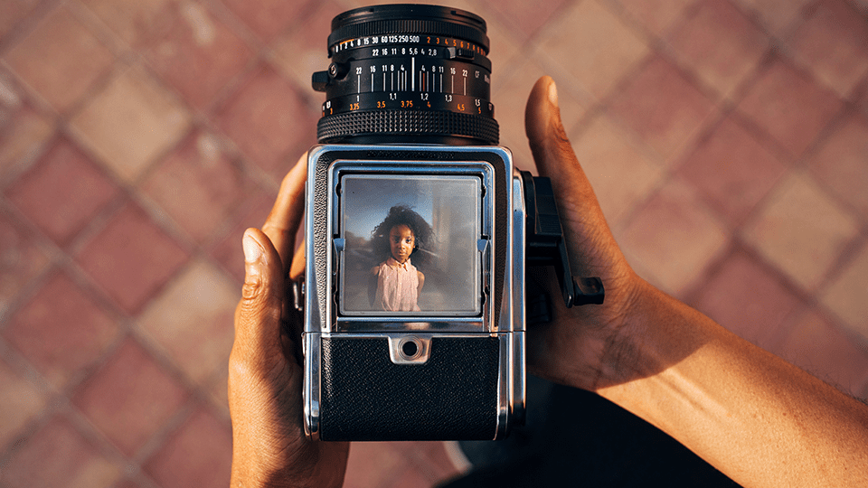 View of a person holding a vintage camera, showing a child's portrait in the viewfinder.